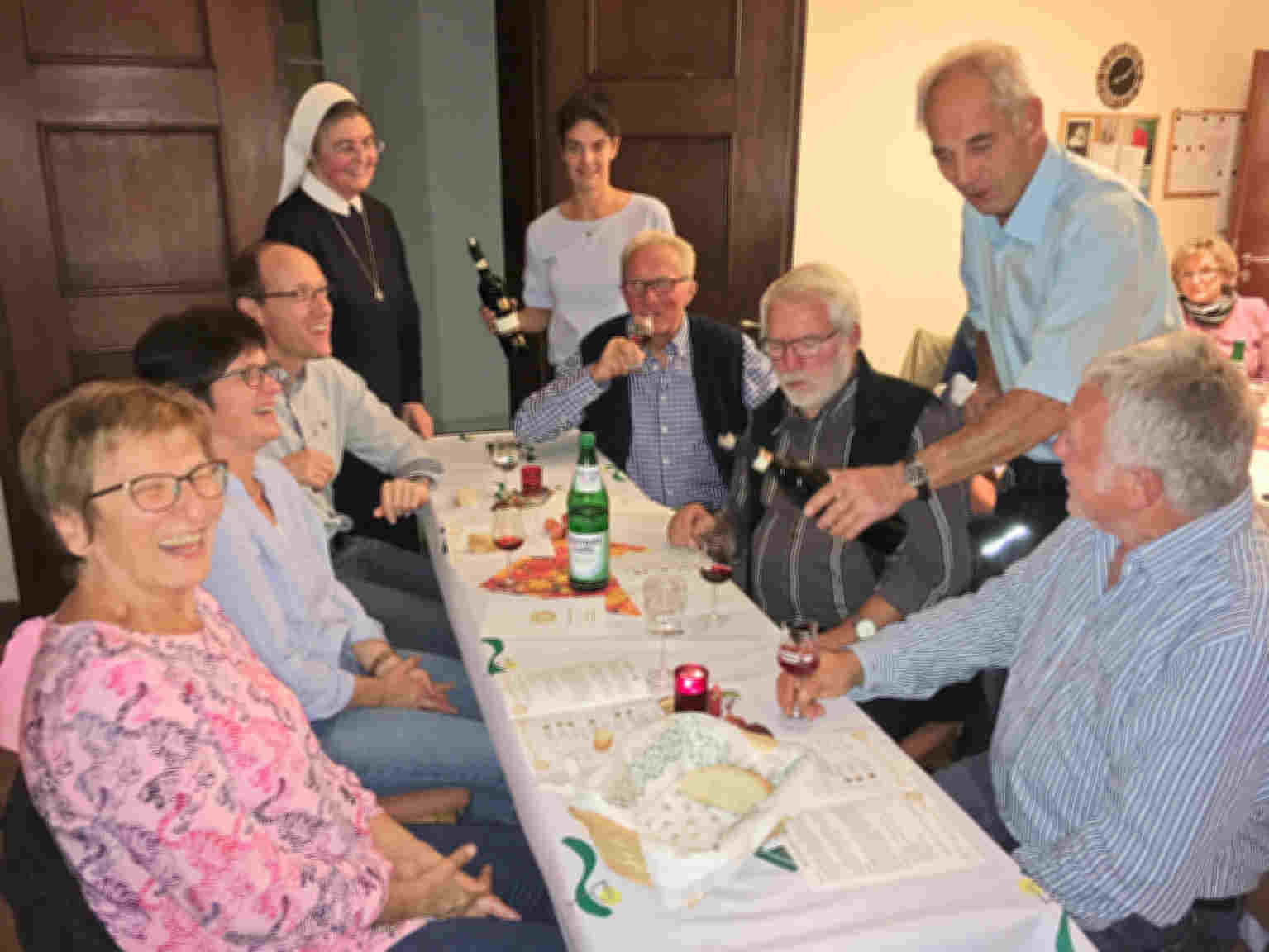 Gäste sitzen am Tisch während der Weinprobe im Mutterhaus der Vinzentinerinnen. Stehend am Tisch sind Schwester Brigitta, die ehemalige Weinkönigin Sandra Engelhard und Winzer Hans Engelhard beim Ausschenken des Weins zu sehen